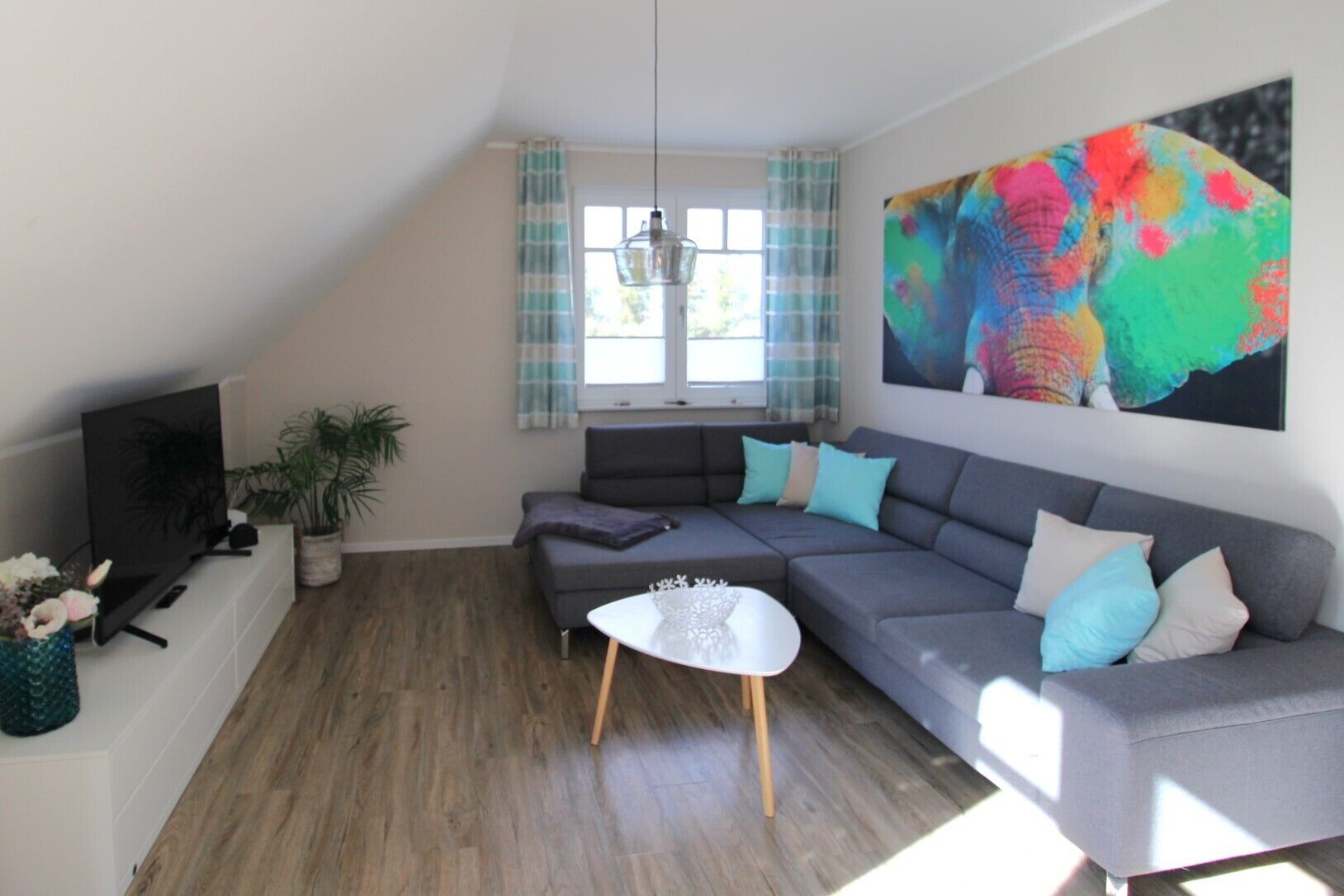 A modern living room with a grey sectional sofa, a small white coffee table, and a flat-screen TV on a white stand.