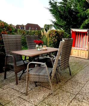 Relax in a serene outdoor space with a table, wicker chairs, and lush greenery.