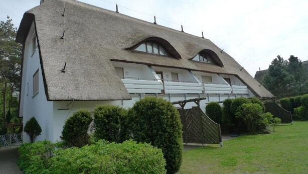 Uma casa tradicional com telhado de colmo, paredes brancas e cerca de madeira.