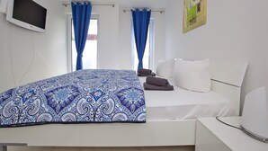 Ett hotellrum med en säng, en platt-TV, två fönster med blå gardiner och en tavla på väggen.