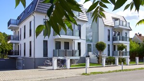 En modern bostadsbyggnad i två våningar med balkonger, en överbyggd entré och ett litet träd på framsidan.