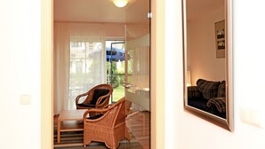 Une pièce dotée d’une porte vitrée donnant sur un balcon, de meubles en osier et d’un tableau encadré accroché au mur.