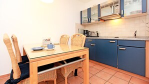 Une cuisine compacte avec une table à manger, des chaises en osier et des meubles de rangement bleus.