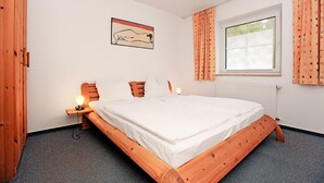 Une chambre à coucher avec un lit en bois, une table de chevet avec une lampe, une fenêtre avec des rideaux et un tableau accroché au mur.