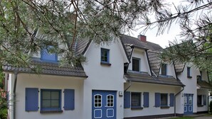 Une rangée de bâtiments blancs aux portes et volets bleus, numérotés 6, 7 et 8, avec un toit en tuiles et un petit jardin devant.
