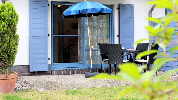 Une terrasse avec une table et des chaises, un parasol bleu et une plante en pot.
