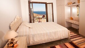 A bedroom with a bed, a nightstand, a lamp, a view of the sea, and a wooden floor. - Nikis seaside house  (KALYMNOS)