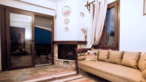 A cozy living room with a sofa, a fireplace, and a sliding glass door leading to an outdoor area. - Nikis seaside house  (KALYMNOS)