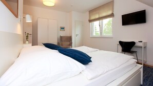 A bedroom with a bed, a chair, a desk, a TV, and a window with curtains.