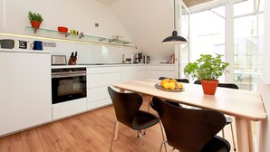 A modern kitchen with white cabinets, a wooden dining table, black chairs, and a potted plant.