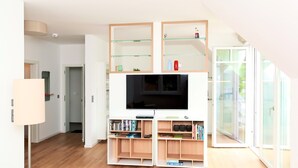 A modern living room with a flat-screen TV, wooden shelving, and a lamp.