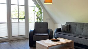 Ein modernes Wohnzimmer mit Couchtisch aus Holz, einer grauen Couch und einem schwarzen Sessel.