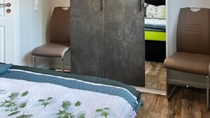 Ein Schlafzimmer mit einem Bett, zwei Stühlen, einem Kleiderschrank und einem Spiegel.