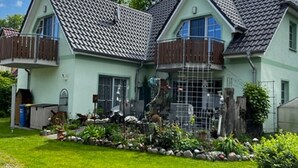 Ein zweistöckiges Haus mit Ziegeldach, einem Balkon im zweiten Obergeschoss und einem gepflegten Garten mit einem Kiesweg.