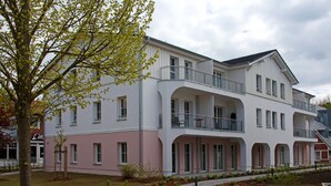A multi-story building with a pink and white facade, balconies, and a landscaped courtyard. - In Unmittelbarer Strandnähe ca. 100m (Ostseebad Wustrow)