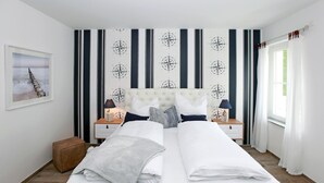 A double bed with white bedding, a tufted headboard, and a bedside table with a lamp. - In Unmittelbarer Strandnähe ca. 100m (Ostseebad Wustrow)