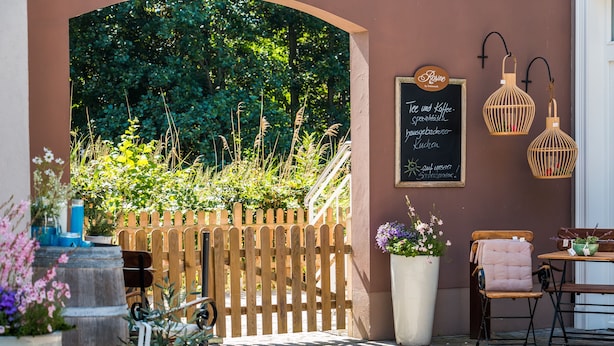 Ein Sitzbereich im Freien mit Holzzaun, einer Kreidetafel mit Speisekarte und zwei hängenden Laternen.