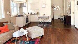 Eine moderne Wohnung mit Küche, Essbereich und Wohnzimmer. Sie verfügt über ein großes Fenster, ein Sofa, einen Couchtisch und einen Teppich.