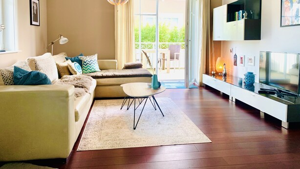 A modern living room with a sofa, a coffee table, a TV, and a large window with curtains. - Haustierfreundlich und in Strandnähe (Ostseebad Wustrow)