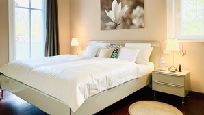 A neatly made bed with white linens, a bedside table with a lamp, and a painting of a flower on the wall. - Haustierfreundlich und in Strandnähe (Ostseebad Wustrow)