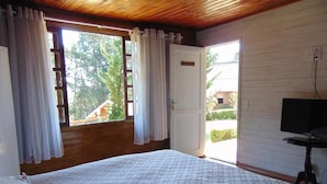 Un dormitorio con una cama grande, un televisor sobre un mueble, techo de madera y una puerta que da al exterior.