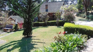 Una casa con techo inclinado, rodeada de un jardín cuidado con diversas plantas y césped.