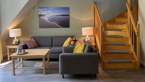 A modern living room with a grey sofa, a wooden coffee table, and a staircase with wooden railings.