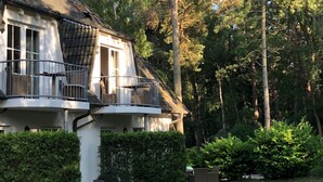 A two-story house with a balcony, surrounded by dense greenery and trees.