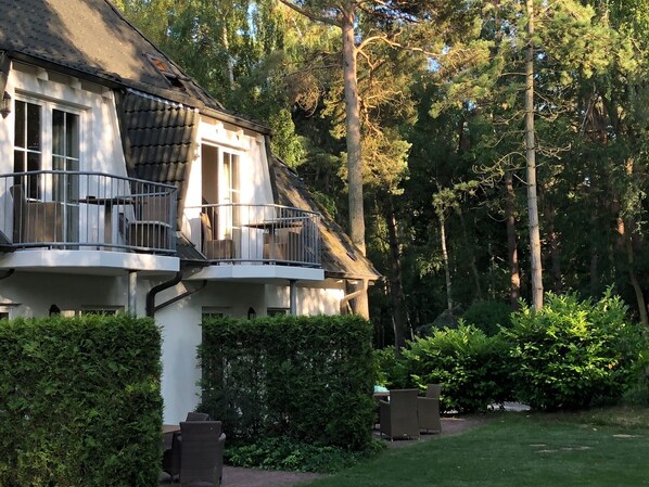 A two-story house with a balcony, surrounded by dense greenery and trees.