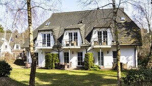 A two-story house with a tiled roof, white exterior walls, and a front porch with outdoor furniture.