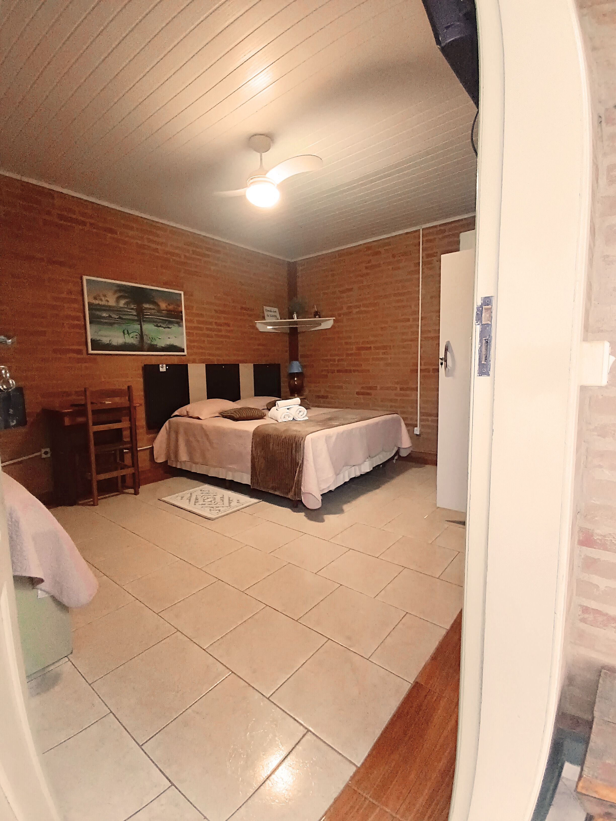 Una habitación con cama, escritorio, silla, un cuadro en la pared y ventilador de techo.