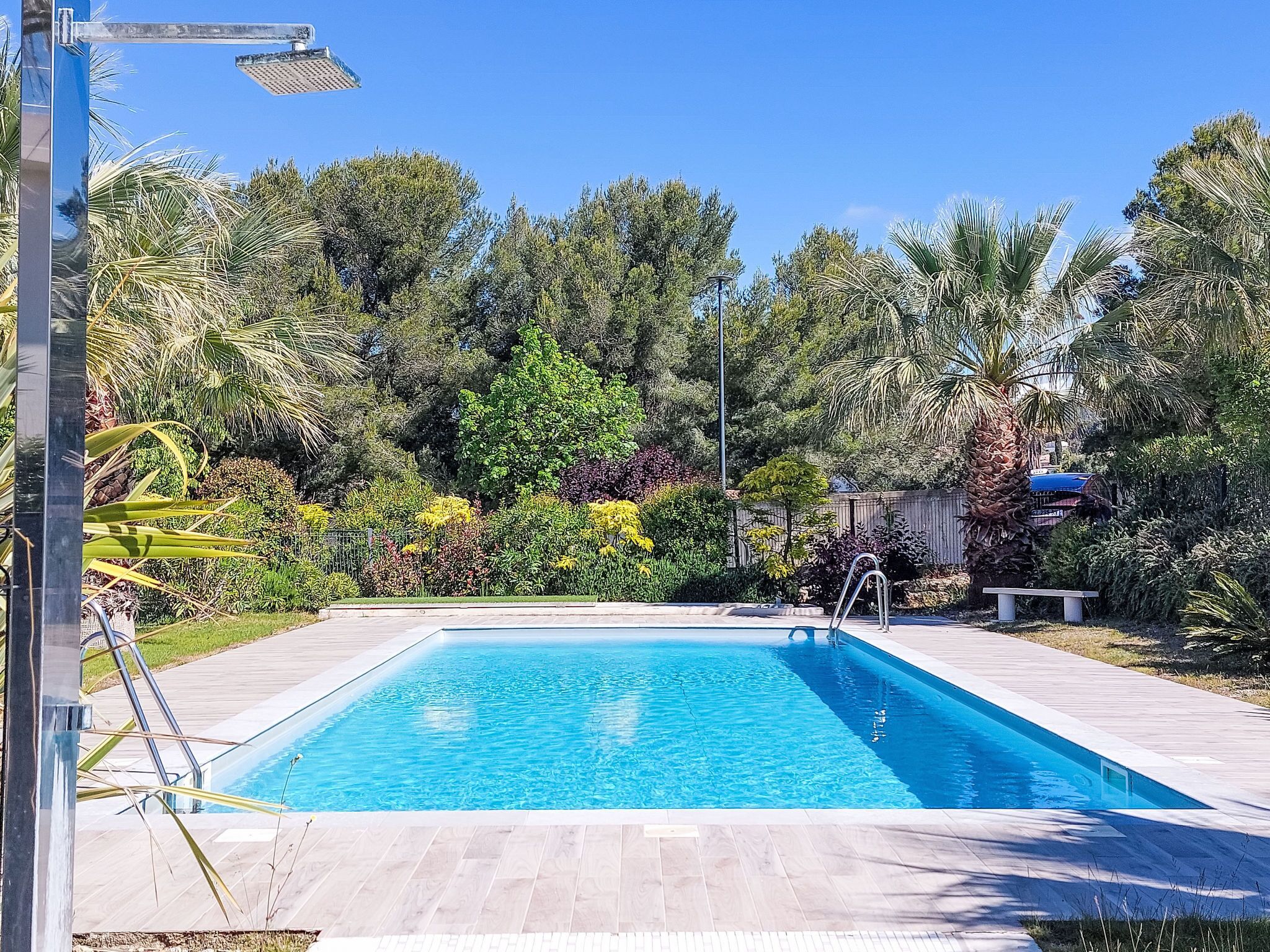 A rectangular swimming pool with clear blue water, surrounded by a wooden deck and lush greenery.