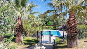 A pool area with palm trees, a fenced pool, and a building in the background. - Les Terrasses d'Azur by Interhome (Sanary sur Mer)