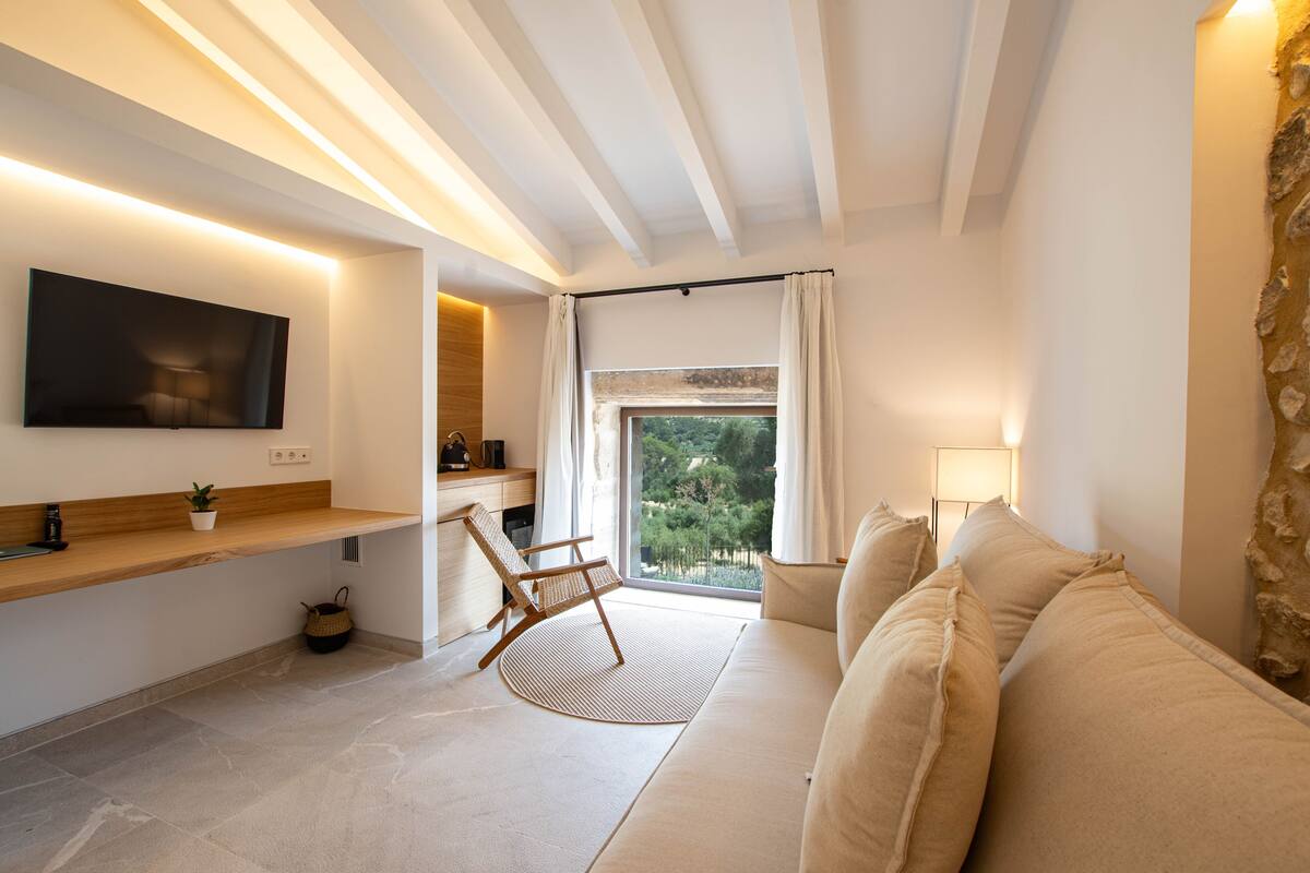 Una sala de estar moderna con un sofá, una silla de madera, un televisor de pantalla plana, una ventana con cortinas y una pared de piedra.
