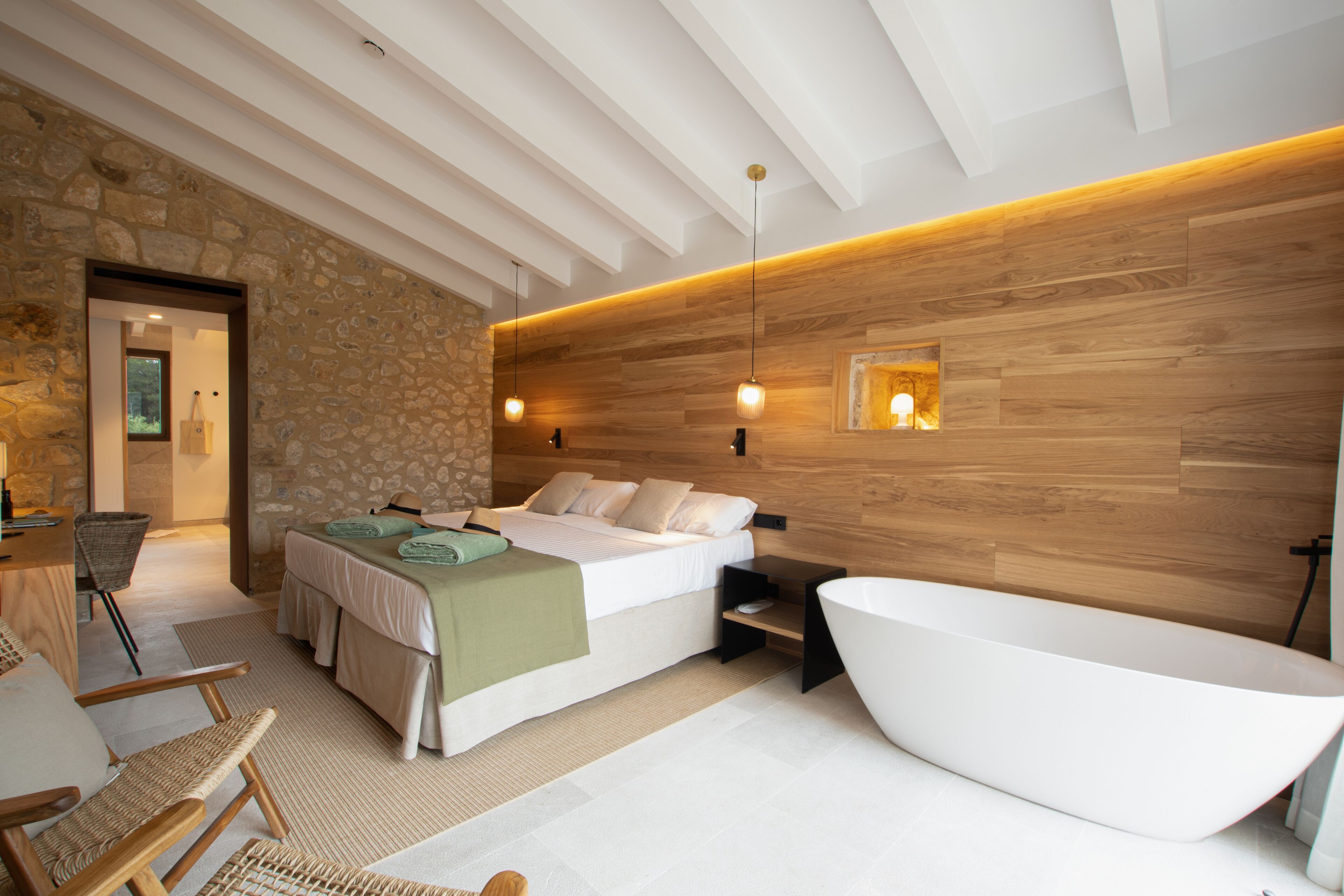 Un dormitorio moderno con una cama grande, una bañera independiente y una pared de piedra.