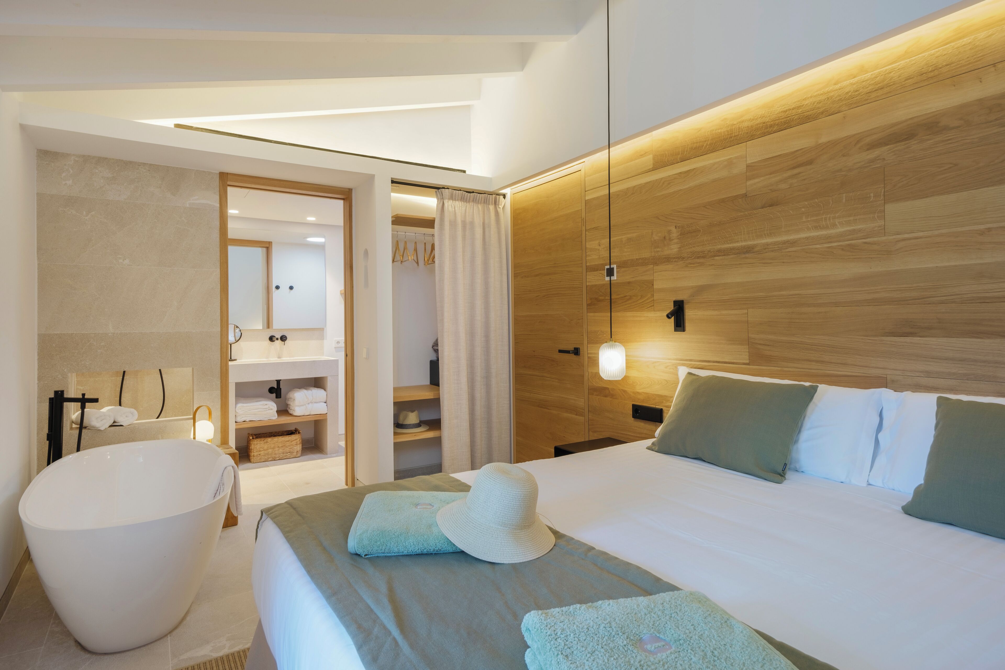 Habitació d'hotel moderna amb una banyera gran, un llit ben fet amb almoçades i un panell de fusta.