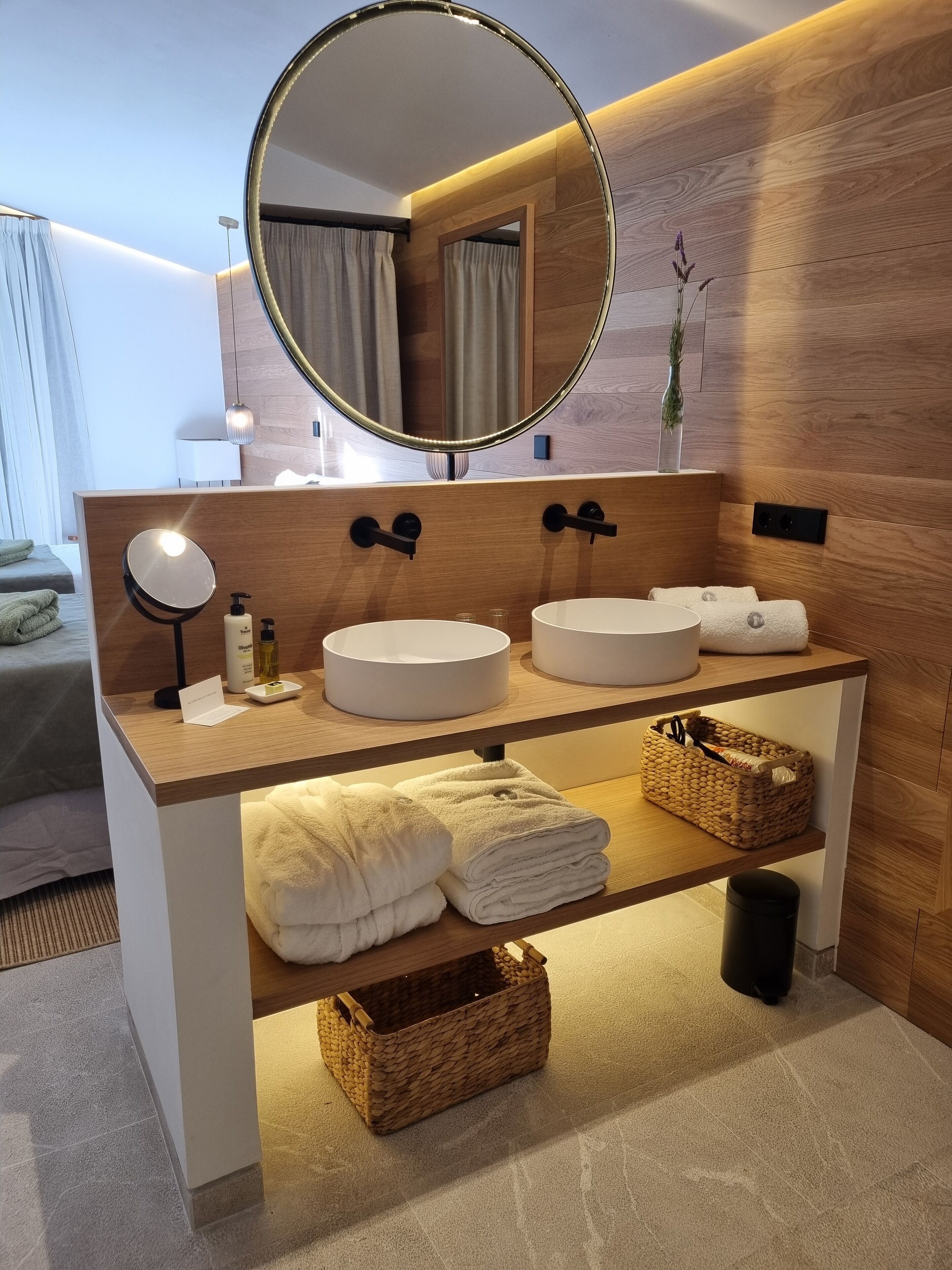 Un baño moderno con tocador de madera, dos lavamanos, un espejo grande y un perchero para toallas.
