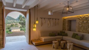 Un salon moderne avec un mur en pierre, un canapé avec des coussins, un luminaire suspendu et une vue sur l’extérieur.