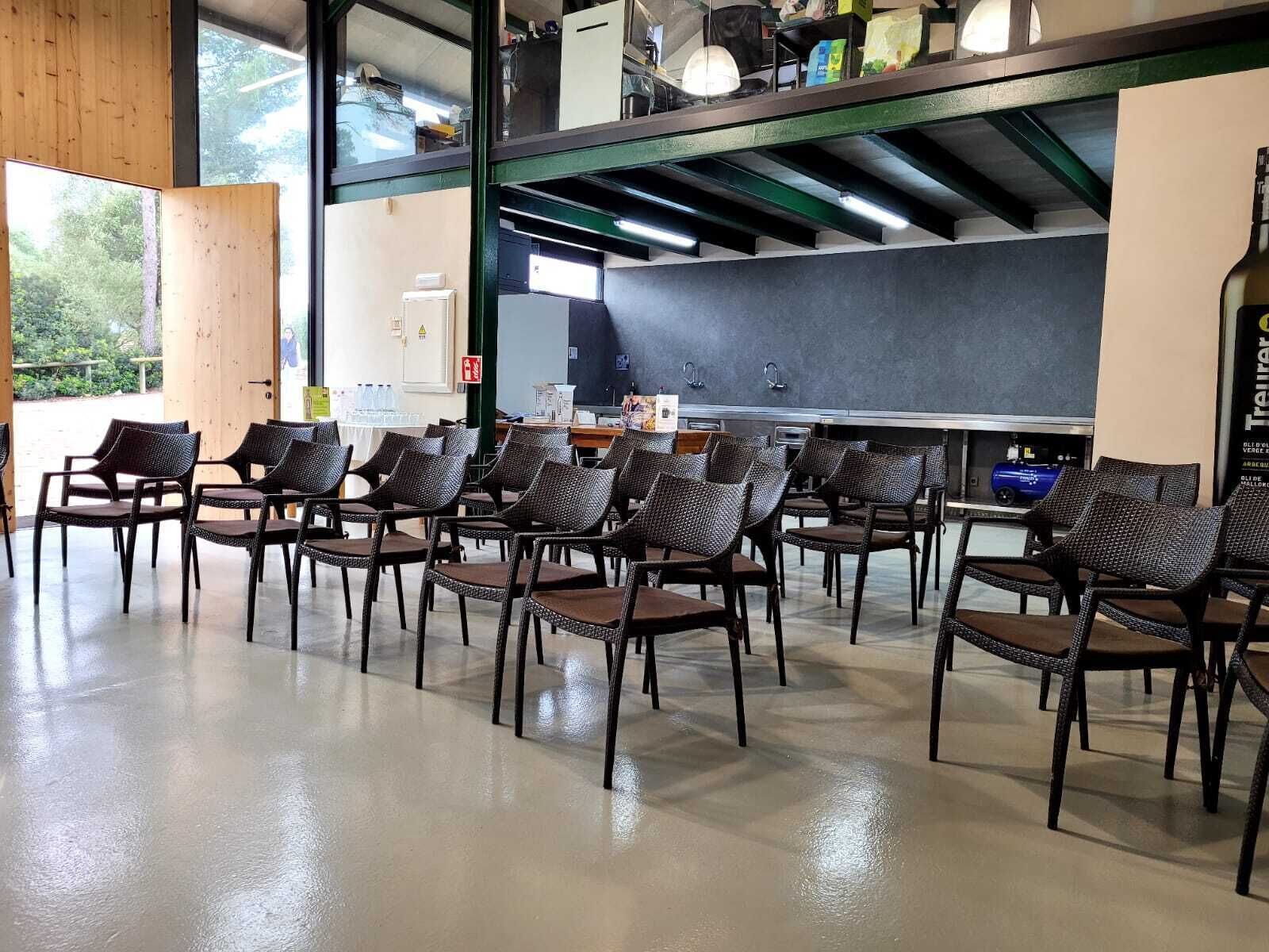 A spacious room with a long table and chairs, a chalkboard, and a large window with a view of greenery.