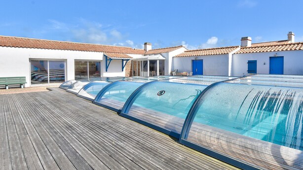 Una hilera de piscinas cubiertas de vidrio sobre una terraza de madera, con edificios al fondo.