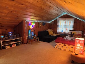 Una habitación acogedora con paredes de madera, un letrero de neón, un sofá, una cama y máquinas de juegos arcade.