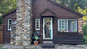 A log cabin with a stone chimney, a front porch, and a window with a flower box.