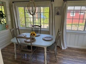 Comedor con una mesa dispuesta para cuatro personas, sillas, una araña y ventanas amplias con cortinas.