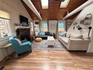 Un soggiorno accogliente con camino, una poltrona blu, un divano bianco e un soffitto in legno.