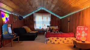 A cozy attic bedroom with wooden walls, a neon sign, a gaming console, a bed with a Hogwarts-themed blanket, and a decorative lamp. - Amazing lake house with everything you need!  (Ashford)