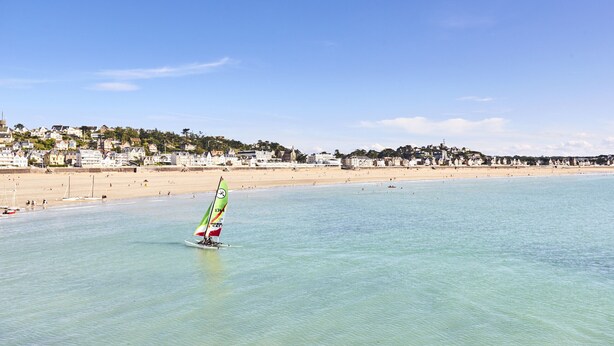 A beach with a sailboat, clear water, and a coastal town in the background. - Ecapade for 4 in Pléneuf-Val-André (Pléneuf-Val-André)