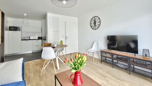 A modern living room with a TV, a red vase with flowers, and a dining area with chairs and a table. - Ecapade for 4 in Pléneuf-Val-André (Pléneuf-Val-André)