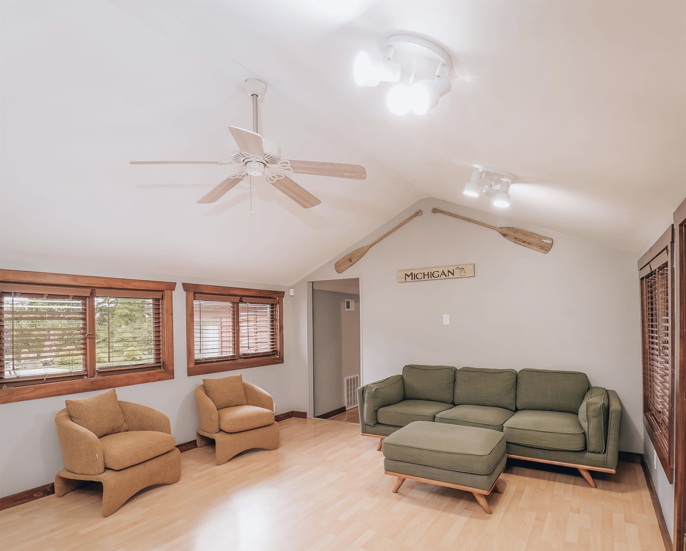 Una habitación amplia con ventilador de techo, un sofá seccional verde y dos sillones marrones.