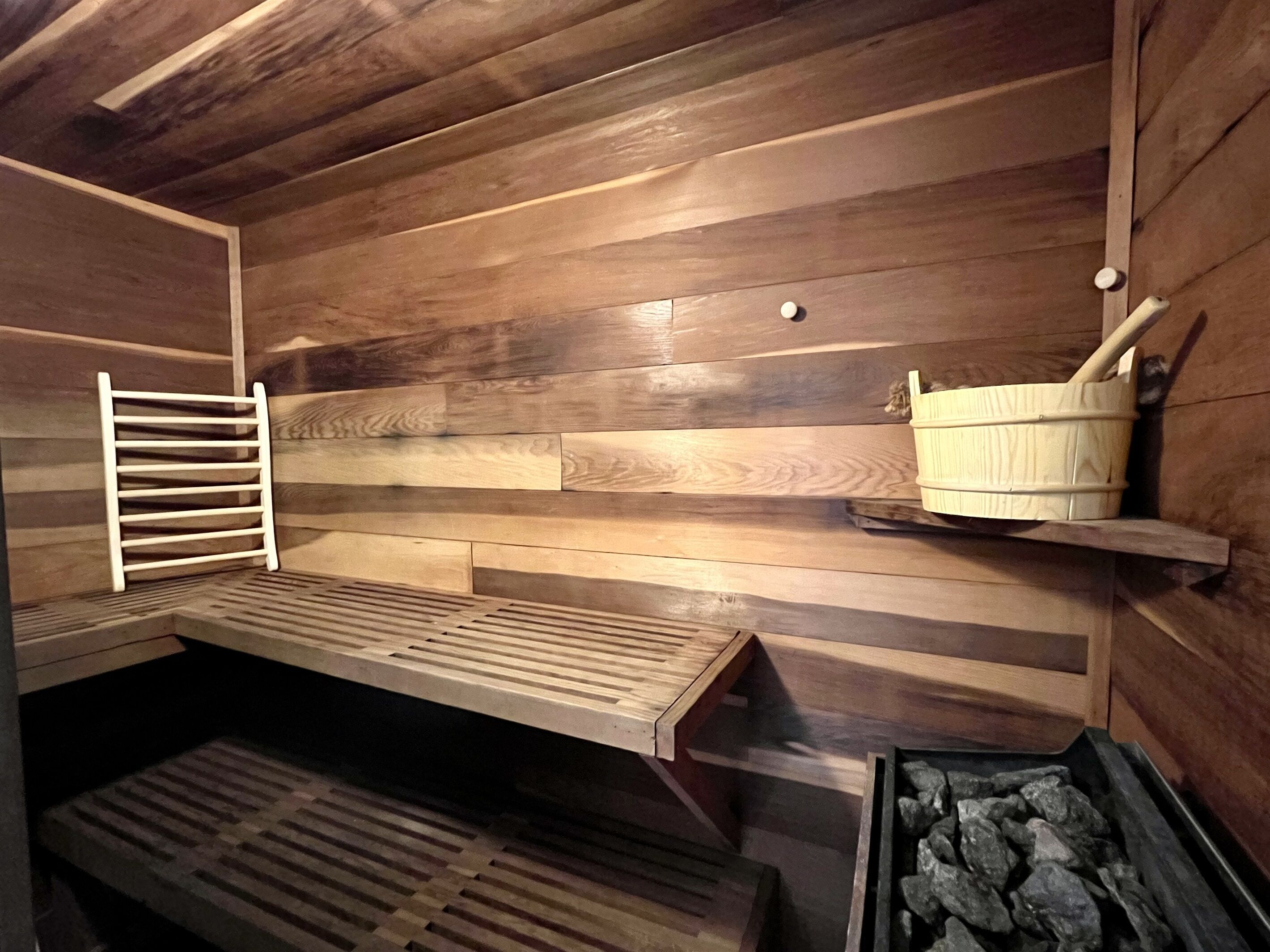 Un sauna avec des bancs en bois, un banc à lattes et un seau posé sur une étagère.