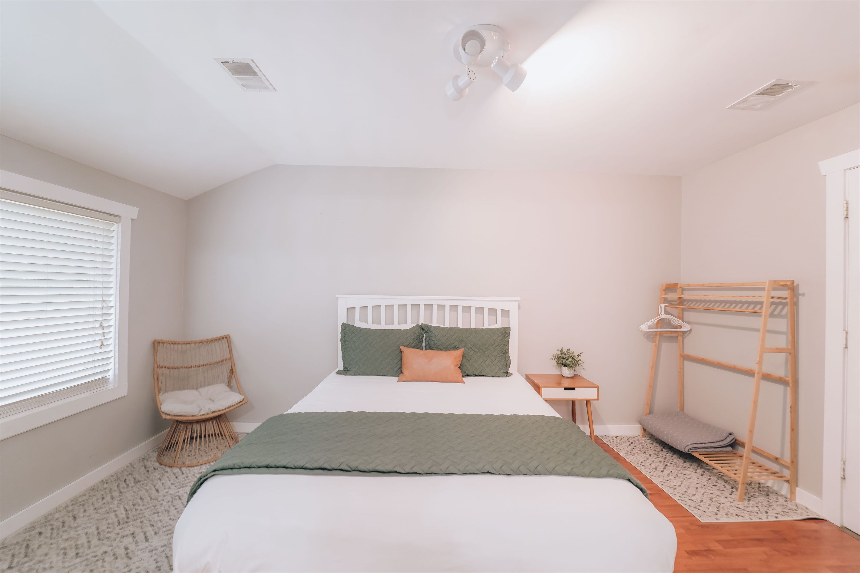 Un dormitorio con cama, una silla, una mesita de noche, una escalera y una ventana con persianas.